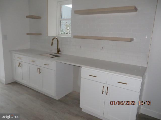 kitchen featuring white cabinets, decorative backsplash, light wood-type flooring, and sink