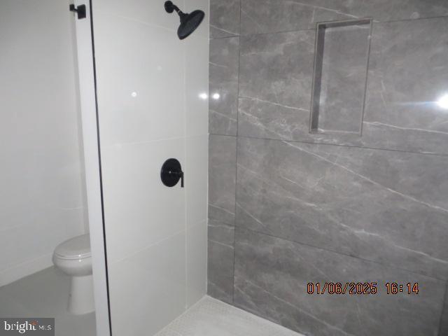 bathroom with a tile shower and toilet