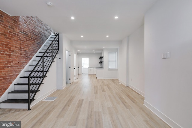 hallway with sink, brick wall, and light hardwood / wood-style flooring