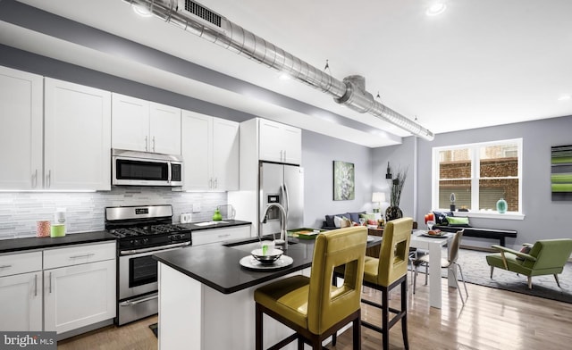 kitchen featuring sink, stainless steel appliances, a kitchen bar, a center island with sink, and white cabinets