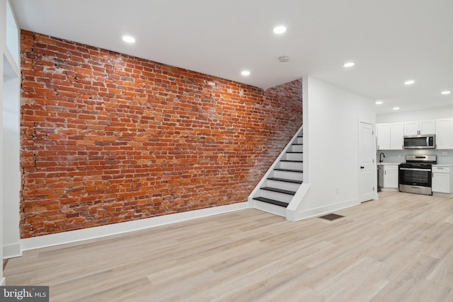 unfurnished living room with light hardwood / wood-style flooring, brick wall, and sink