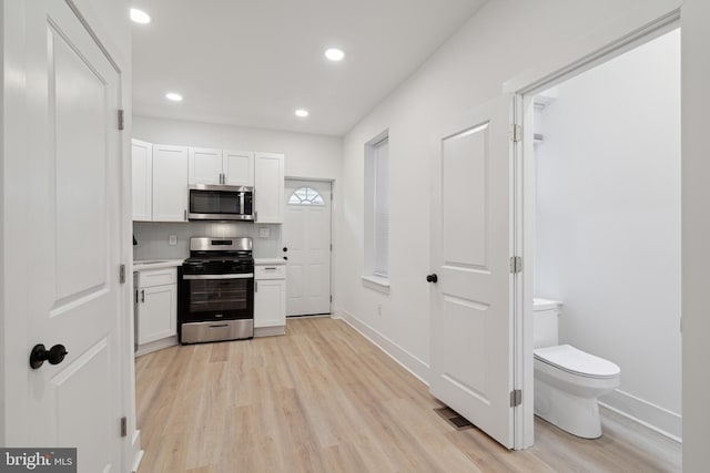 kitchen featuring tasteful backsplash, white cabinetry, light wood-type flooring, and appliances with stainless steel finishes