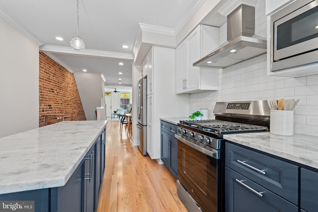 kitchen featuring blue cabinetry, stainless steel appliances, wall chimney range hood, brick wall, and decorative backsplash