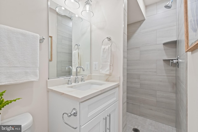 bathroom with a tile shower, vanity, and toilet