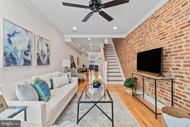 living room with wood-type flooring, ceiling fan, ornamental molding, and brick wall