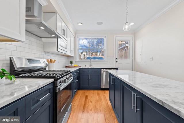 kitchen with white cabinets, wall chimney range hood, sink, decorative light fixtures, and stainless steel appliances