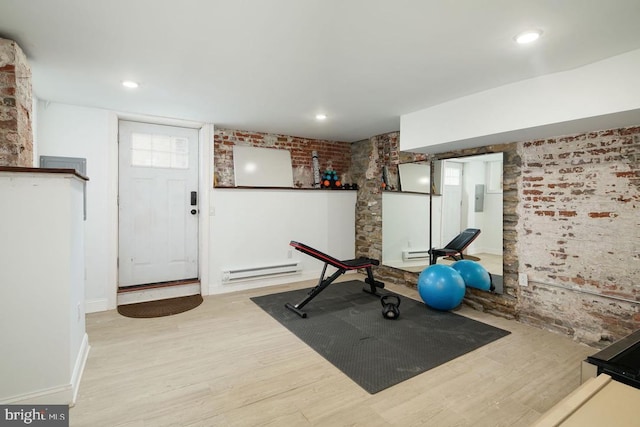 workout room featuring light wood-type flooring, a baseboard heating unit, and brick wall