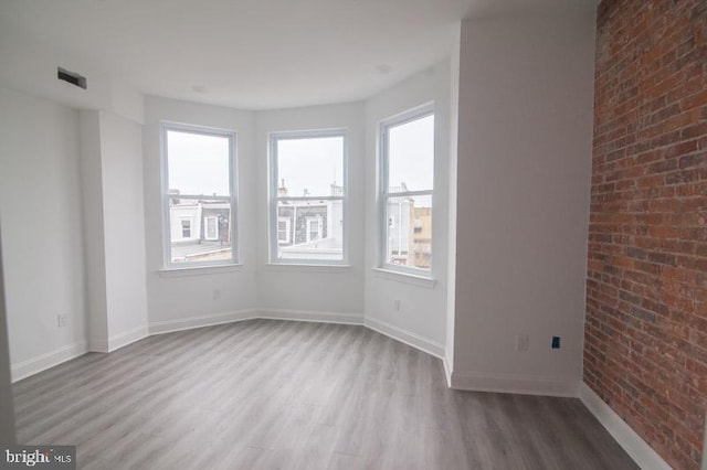 unfurnished room with hardwood / wood-style flooring and brick wall