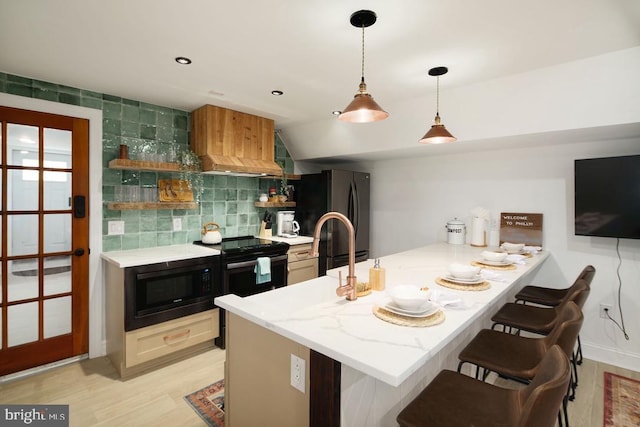 kitchen featuring a breakfast bar, backsplash, black appliances, light hardwood / wood-style flooring, and kitchen peninsula