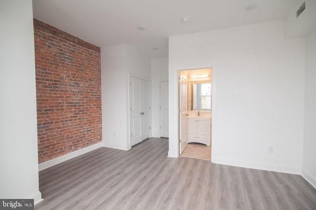 unfurnished bedroom featuring light hardwood / wood-style floors, brick wall, and ensuite bath