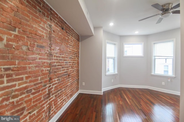 spare room featuring dark hardwood / wood-style floors, ceiling fan, and brick wall