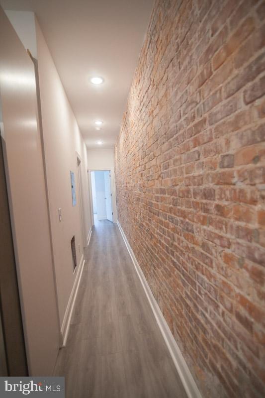 hall with brick wall and wood-type flooring