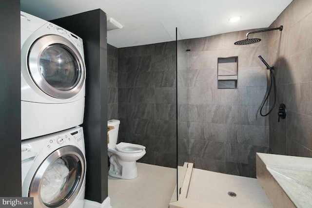 bathroom with tiled shower, stacked washer and dryer, toilet, and tile walls