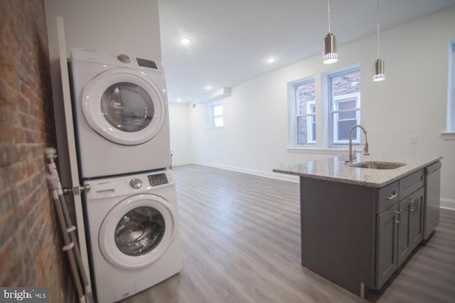 clothes washing area with dark wood-type flooring, sink, and stacked washer and dryer