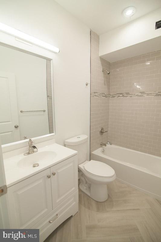 full bathroom featuring parquet floors, vanity, tiled shower / bath combo, and toilet