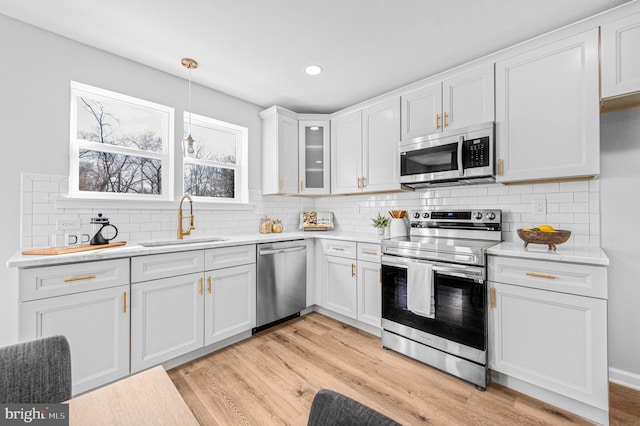 kitchen with stainless steel appliances, sink, pendant lighting, white cabinets, and light hardwood / wood-style floors