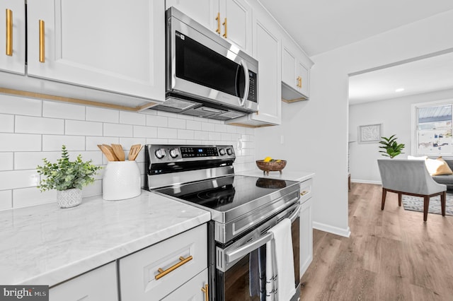 kitchen featuring light stone countertops, light hardwood / wood-style flooring, decorative backsplash, white cabinets, and appliances with stainless steel finishes