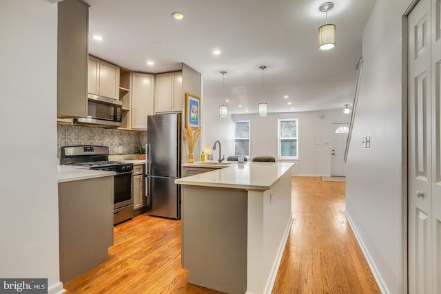 kitchen with sink, light hardwood / wood-style flooring, appliances with stainless steel finishes, decorative light fixtures, and kitchen peninsula