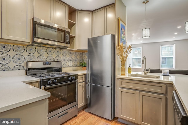 kitchen featuring decorative backsplash, appliances with stainless steel finishes, light wood-type flooring, sink, and decorative light fixtures