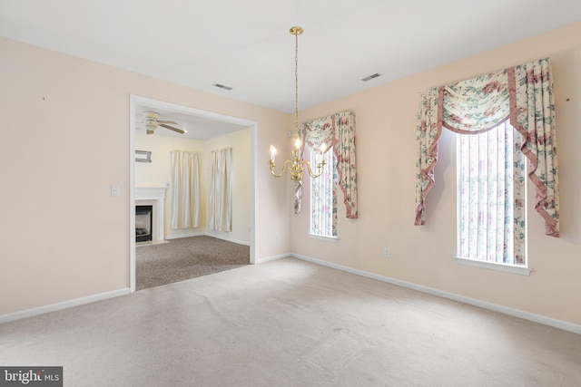 carpeted empty room featuring a wealth of natural light and ceiling fan with notable chandelier