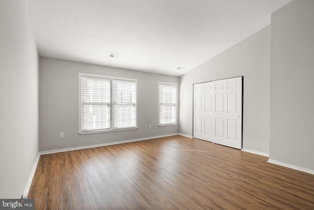 unfurnished bedroom with hardwood / wood-style flooring, a closet, lofted ceiling, and multiple windows