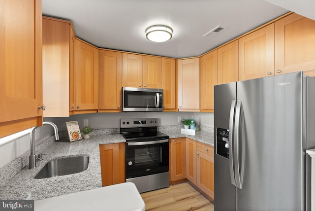 kitchen with light brown cabinetry, sink, light stone counters, appliances with stainless steel finishes, and light hardwood / wood-style floors