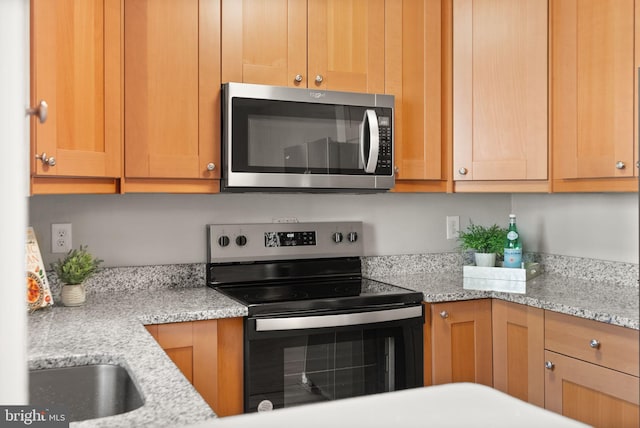 kitchen with appliances with stainless steel finishes, sink, and light stone counters