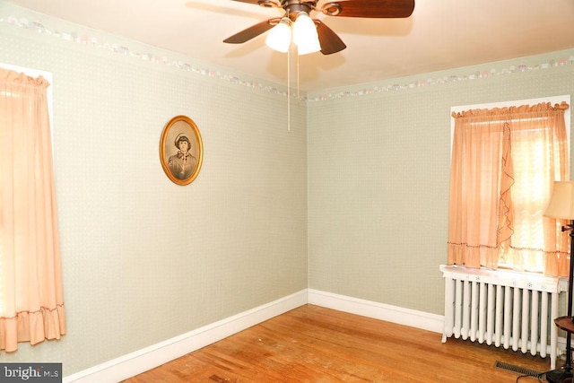 spare room with hardwood / wood-style floors, ornamental molding, radiator heating unit, and ceiling fan