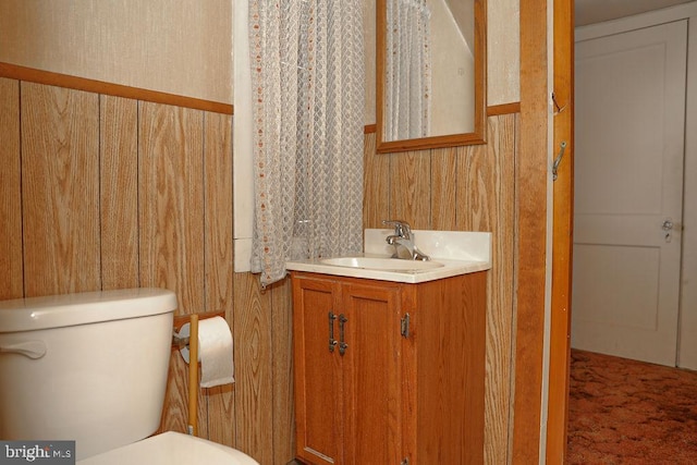 bathroom featuring vanity, toilet, and wood walls