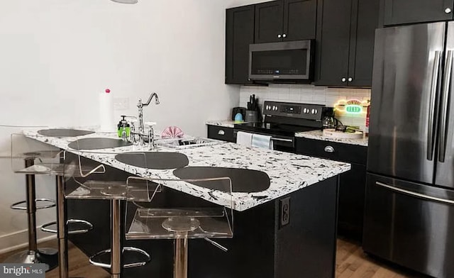 kitchen featuring a kitchen breakfast bar, wood-type flooring, an island with sink, and appliances with stainless steel finishes