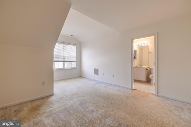 unfurnished bedroom with ensuite bath, light colored carpet, and lofted ceiling