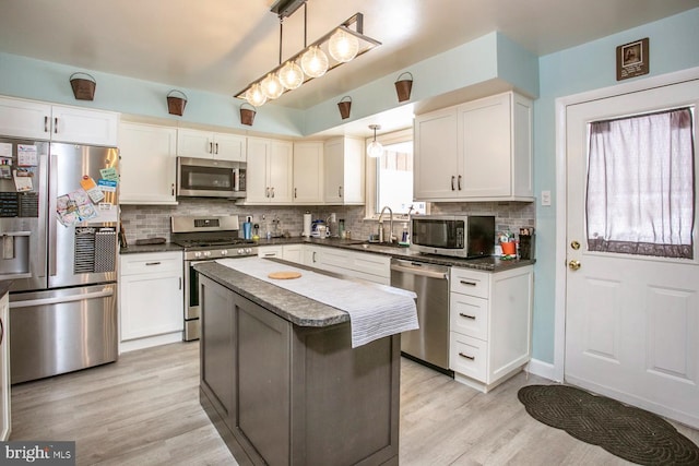 kitchen featuring stainless steel appliances, sink, pendant lighting, white cabinets, and a kitchen island