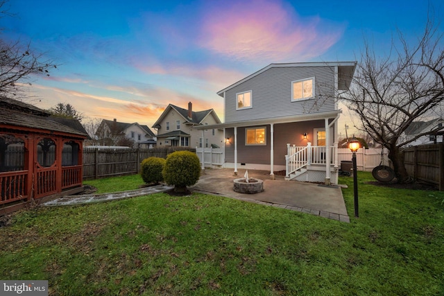 back house at dusk featuring a lawn, a patio area, and an outdoor fire pit