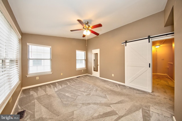 unfurnished bedroom with ceiling fan, a barn door, and carpet floors