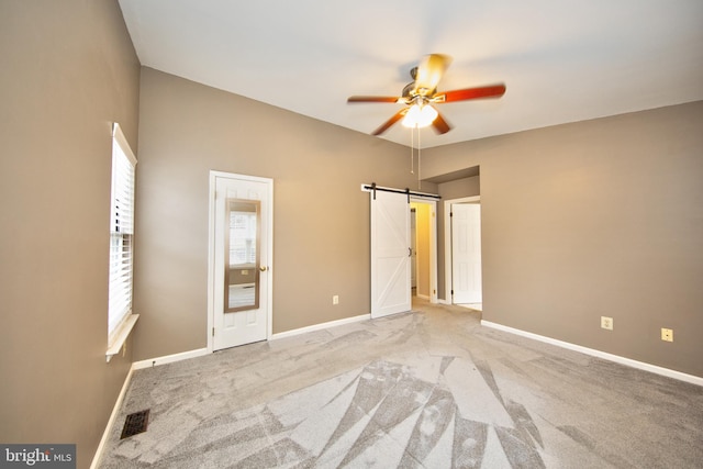 unfurnished bedroom with light carpet, a barn door, and ceiling fan