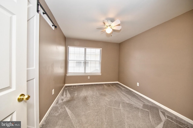 unfurnished room with a barn door, ceiling fan, and carpet floors