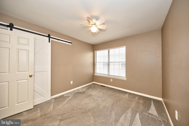 unfurnished bedroom with ceiling fan, a barn door, and carpet floors