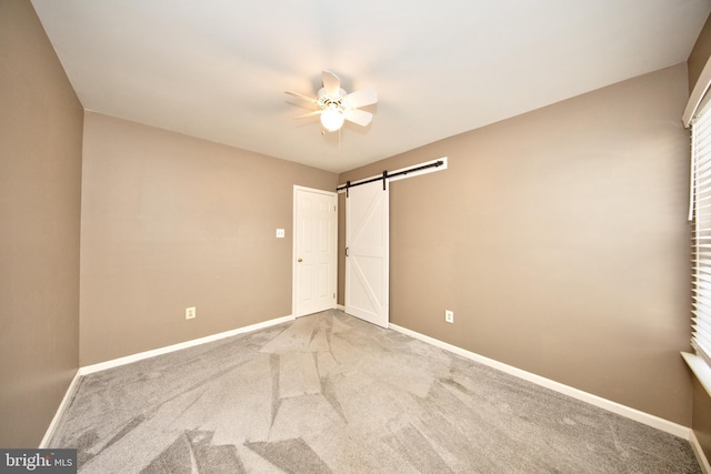 unfurnished bedroom with carpet, ceiling fan, and a barn door