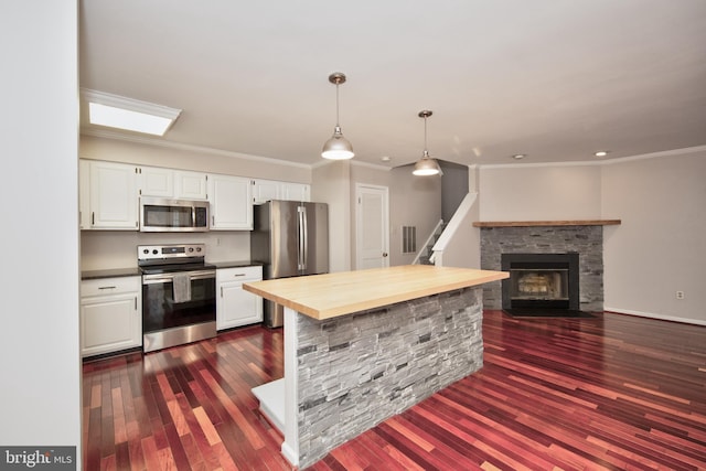 kitchen featuring white cabinets, appliances with stainless steel finishes, hanging light fixtures, and a fireplace