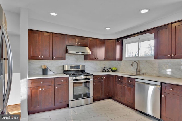 kitchen with decorative backsplash, appliances with stainless steel finishes, light countertops, under cabinet range hood, and a sink