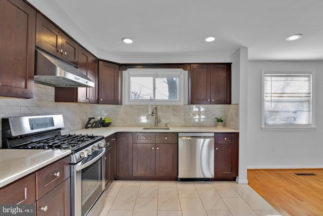 kitchen featuring tasteful backsplash, light countertops, appliances with stainless steel finishes, a sink, and under cabinet range hood