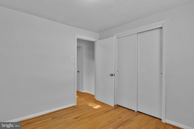 unfurnished bedroom featuring light wood-style flooring, baseboards, and a closet