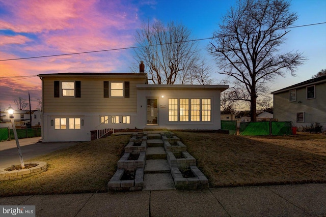 tri-level home with a chimney, stucco siding, concrete driveway, a front yard, and fence