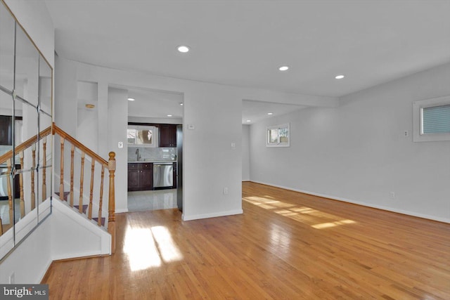 unfurnished living room with recessed lighting, a sink, baseboards, stairs, and light wood finished floors