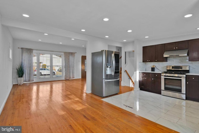 kitchen with under cabinet range hood, stainless steel appliances, dark brown cabinets, light countertops, and tasteful backsplash