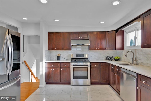 kitchen featuring stainless steel appliances, light countertops, backsplash, a sink, and under cabinet range hood