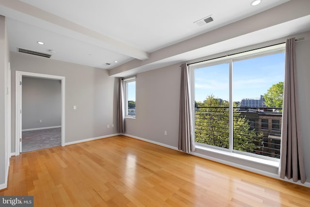 unfurnished room with a wealth of natural light, light hardwood / wood-style flooring, and beamed ceiling