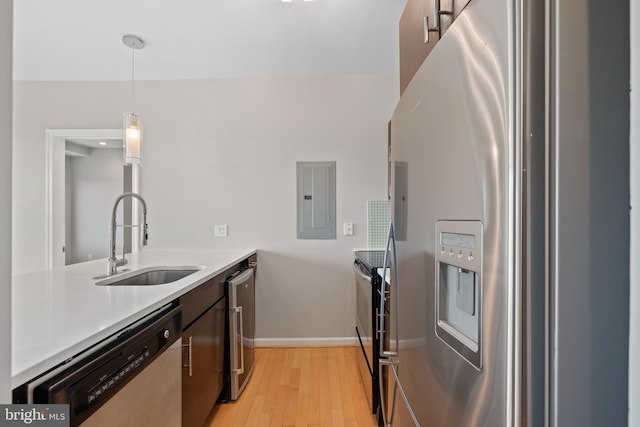 kitchen featuring stainless steel appliances, sink, light hardwood / wood-style flooring, electric panel, and hanging light fixtures