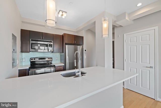 kitchen featuring dark brown cabinetry, sink, hanging light fixtures, stainless steel appliances, and backsplash