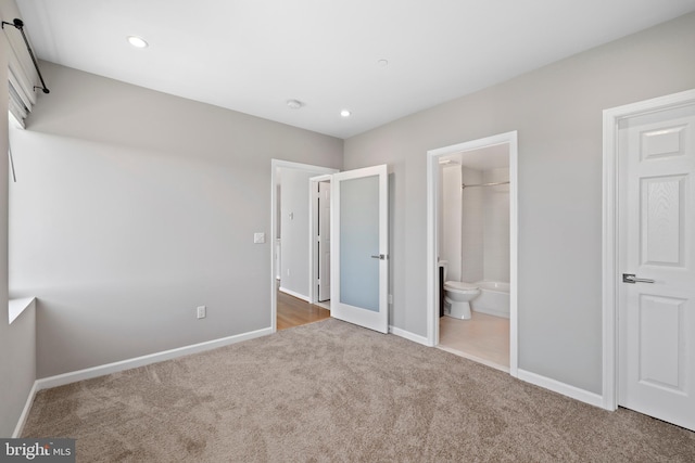 unfurnished bedroom with ensuite bathroom, a walk in closet, and carpet floors